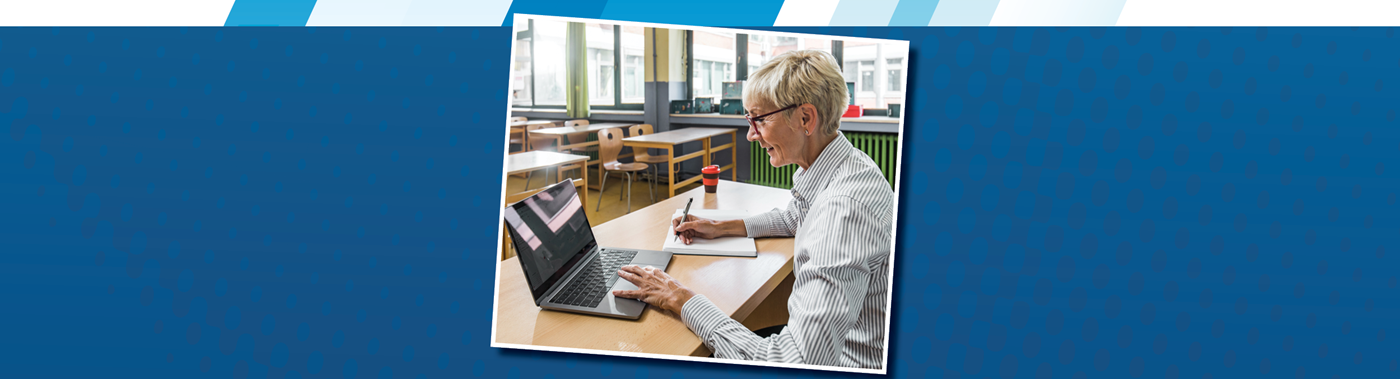 older adult in a classroom working on a laptop and taking notes