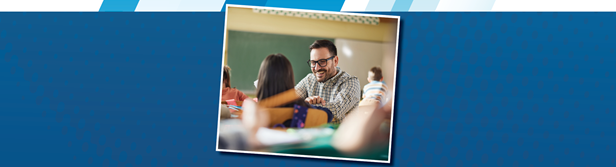smiling teacher sitting at his desk in front of a classroom
