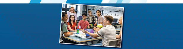Students and teacher discussing something in class. One student sits in front of a laptop.