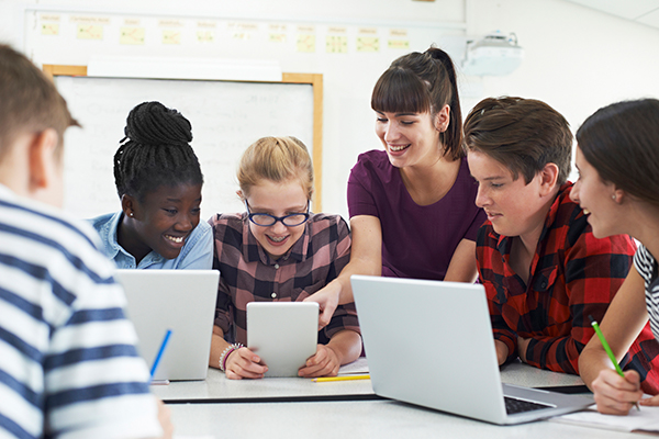 Students learning on computers and tablets with a teacher
