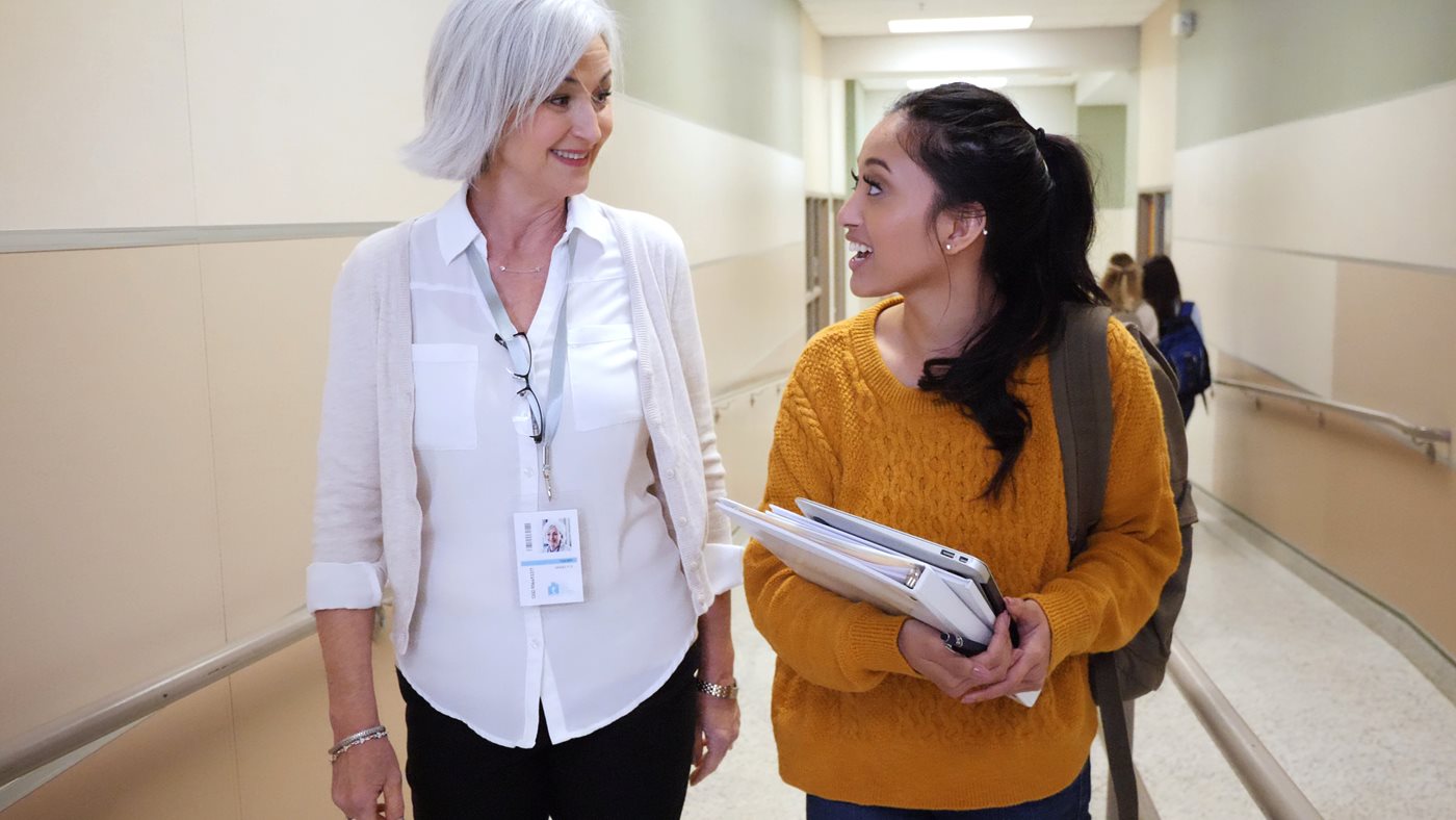 High school student and teacher walk down hallway